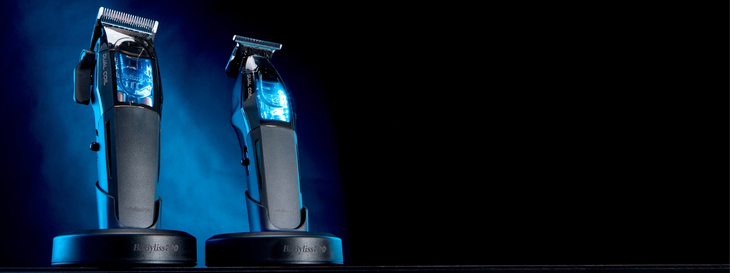 Cortadora de cabello y recortadora BaBylissPRO en posición vertical sobre las bases de carga, iluminadas con una luz azul contra el fondo oscuro.