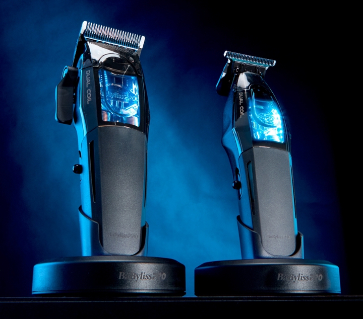 Cortadora de cabello y recortadora BaBylissPRO en posición vertical sobre las bases de carga, iluminadas con una luz azul contra el fondo oscuro.