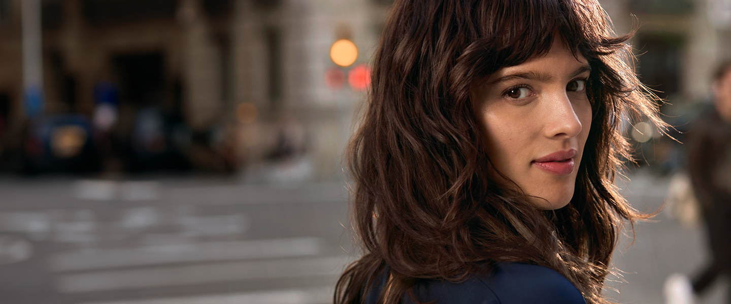 Light‑blue BaBylissPRO hairstyling tools&mdash;including a flat iron, curling wand, and two hair dryers&mdash;are arranged in a radial display on top of white textured pedestals, set against a solid light‑blue background with scattered ice cubes for a cool‑toned aesthetic