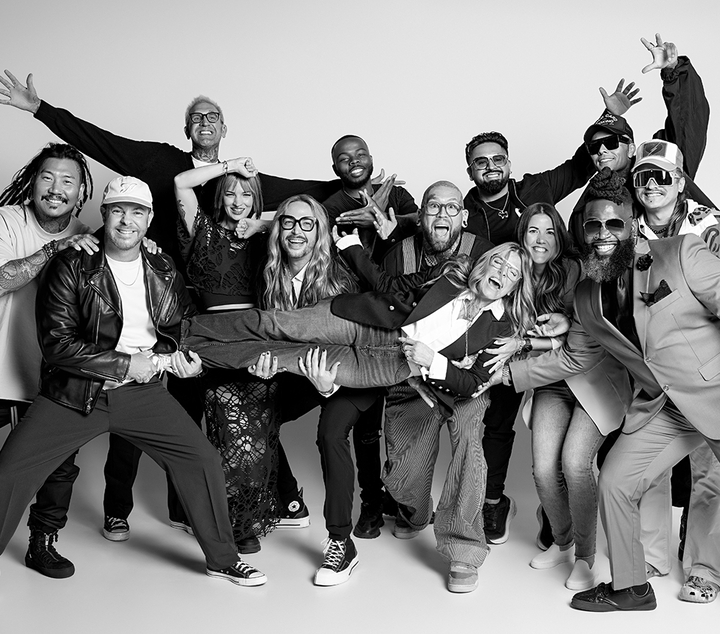 Black‑and‑white group photo of professional hair stylists, barbers, and educators in a playful studio pose